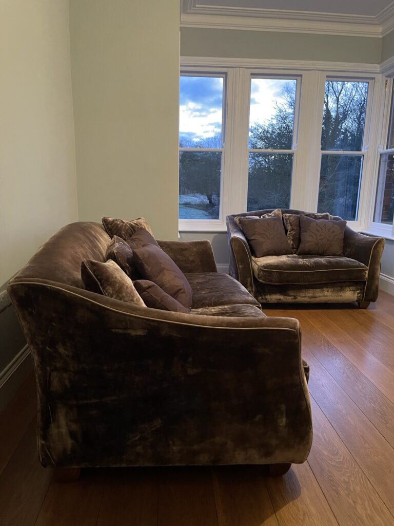 Two large brown velvet sofas in a bay window, the flat velvet visibly crushed all over